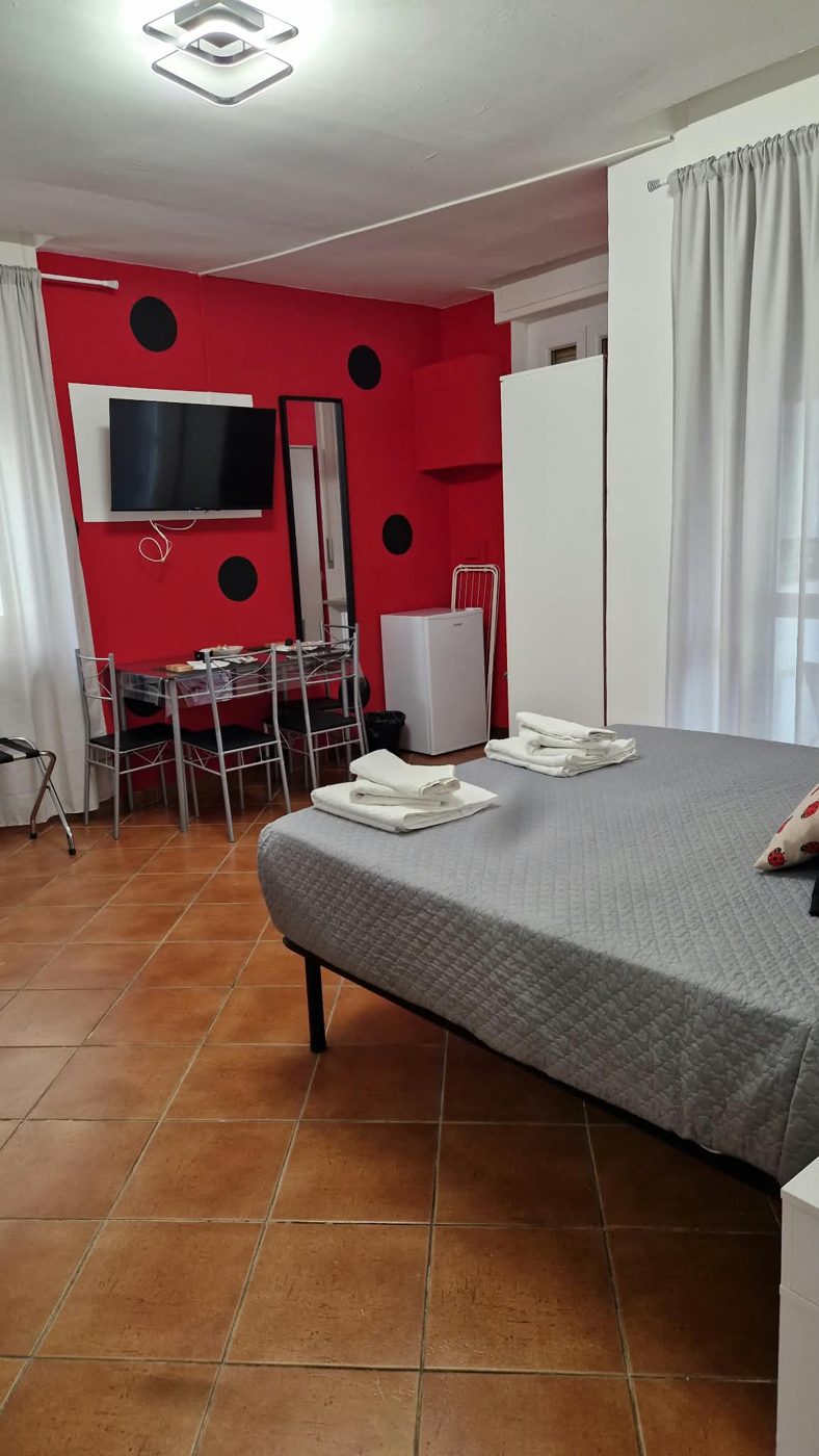 Camera Coccinella: parete rossa a pois neri con TV, specchio, mini frigo e tavolo per quattro